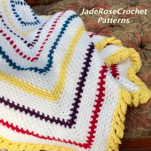 Puede incluir: Una manta de crochet blanca con un borde de rayas de colores. El borde presenta rayas rojas, amarillas, azul verdoso, moradas y amarillas. La manta tiene un borde de crochet amarillo.
