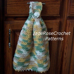 May include: A crocheted kitchen towel with a button and loop for hanging. The towel is made in a striped pattern of beige, green, and yellow yarn. The towel is hanging on a wooden cabinet door. The text "JadeRoseCrochet Patterns" is visible in the image.