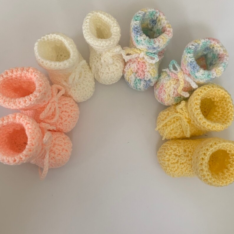 May include: Set of six crocheted baby booties in pink, yellow, and white with pastel rainbow patterns.