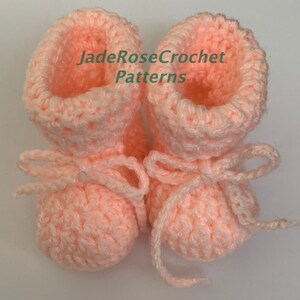 May include: A pair of pink crocheted baby booties with white ties. The booties have a textured stitch pattern and are tied with a bow at the top. The text "JadeRoseCrochet Patterns" is visible on the image.