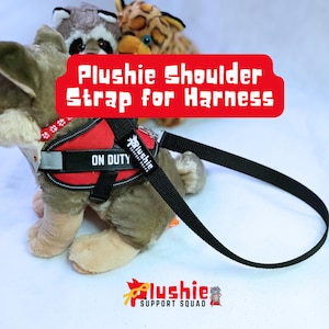 Puede incluir: Un perro de peluche con un arnés rojo y negro con el texto "ON DUTY". Una correa de hombro negra está unida al arnés. La imagen también incluye el texto "Plushie Shoulder Strap for Harness" y el logotipo "Plushie Support Squad".