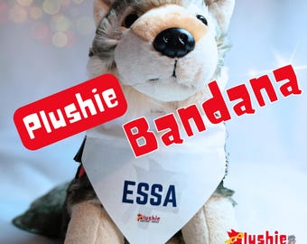 May include: A plush wolf toy wearing a white triangular bandana with the text ESSA printed in dark blue. The text Plushie Bandana is overlaid in red. A small logo with the text Plushie Support Squad is visible on the bandana and bottom right.