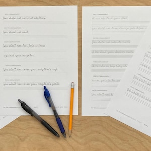 May include: Four sheets of white paper with handwritten text, likely scripture or a similar passage, are arranged on a wooden surface. Two black pens, a blue pen, and a yellow pencil are also present, suggesting a focus on writing or calligraphy.