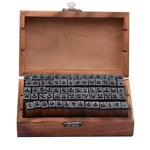 May include: A wooden box with a hinged lid, filled with individual letter stamps. The stamps are black and arranged neatly inside the box. The box is made of a dark brown wood.