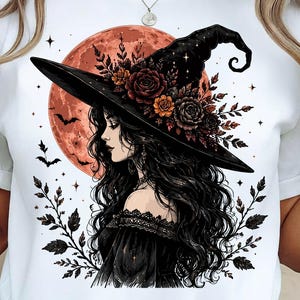 May include: A white t-shirt featuring a graphic illustration of a person with long dark hair wearing a black witch hat adorned with dark red and orange roses. The background shows a large orange moon, flying bats, and dark leafy branches.
