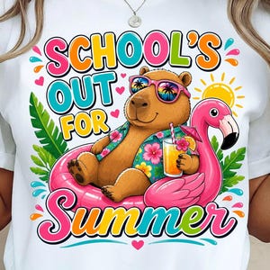 Könnte beinhalten: Ein weißes T-Shirt mit einer Grafik eines braunen Capybaras, das eine Sonnenbrille und ein Blumenhemd trägt und in einem pinken Flamingo-Schwimmring sitzt. Das Capybara hält ein tropisches Getränk. Der Text lautet SCHOOL'S OUT FOR SUMMER.