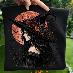 May include: A black fabric square featuring a graphic illustration of a person with long dark hair wearing a wide-brimmed witch hat adorned with orange and dark red roses. A large orange moon and small bats are visible in the background.
