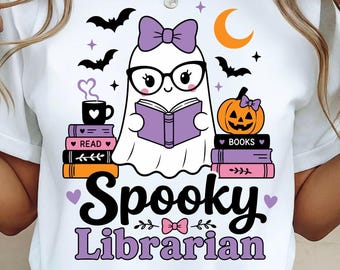 May include: A white t-shirt featuring a graphic of a ghost wearing glasses and a purple bow, reading a book. The design includes stacks of colourful books, a jack-o'-lantern, bats, a crescent moon, and the text Spooky Librarian in black and purple.