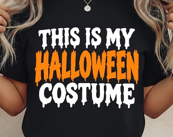 May include: A black short-sleeved t-shirt featuring the white and orange text "THIS IS MY HALLOWEEN COSTUME" printed on the front. The words "THIS IS MY" and "COSTUME" are in a white dripping font, while "HALLOWEEN" is in a bright orange brush font.