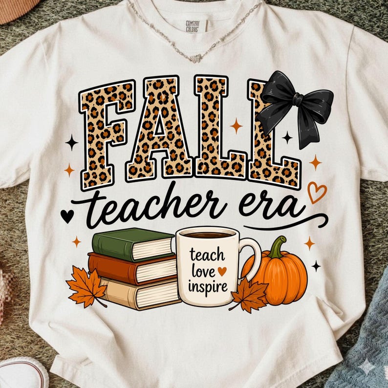 Puede incluir: Una camiseta color crema con la palabra FALL en estampado de leopardo y un lazo negro. Debajo, el texto dice teacher era. El dise&ntilde;o incluye una pila de tres libros, una taza de caf&eacute; con el texto teach love inspire y una calabaza.