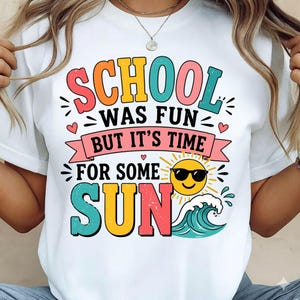 May include: White t-shirt with a colorful graphic that reads "SCHOOL WAS FUN BUT IT'S TIME FOR SOME SUN." The design includes a smiling sun wearing sunglasses, a wave, and hearts.