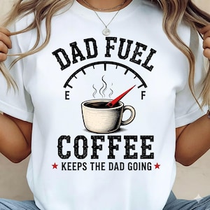 以下が含まれることがあります： グラフィックデザインの白いTシャツ。「DAD FUEL」の文字がコーヒーカップの画像の上にあり、その下に「COFFEE」の文字があります。「KEEPS THE DAD GOING」の文字が一番下にあります。デザインはヴィンテージ風です。