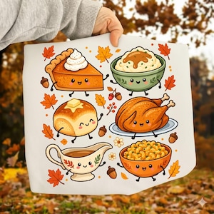 Puede incluir: Una superficie de tela blanca con un estampado gráfico colorido de alimentos antropomórficos de Acción de Gracias, que incluye una rebanada de pastel de calabaza, puré de patatas, un pavo asado, un panecillo, una salsera y macarrones con queso.
