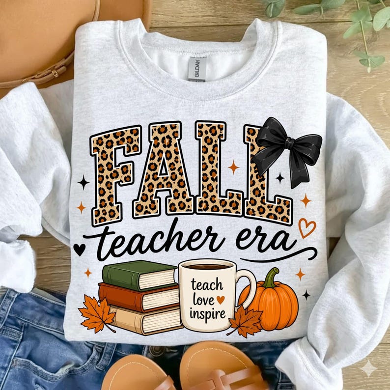 Puede incluir: Una sudadera gris claro de cuello redondo con el texto FALL en estampado de leopardo con un lazo negro, el texto teacher era, una pila de tres libros, una taza con el texto teach love inspire y un gr&aacute;fico de una calabaza naranja.