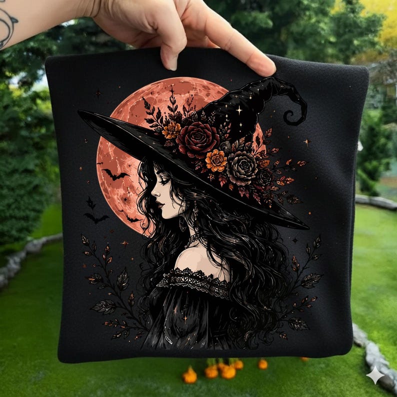 May include: A black fabric square featuring a graphic illustration of a person with long dark hair wearing a wide-brimmed witch hat adorned with orange and dark red roses. A large orange moon and small bats are visible in the background.