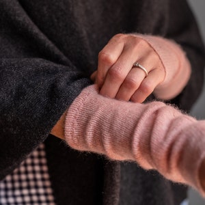 May include: A close-up of a person wearing a dark grey sweater with a pink knitted sleeve. The person is wearing a ring on their finger.
