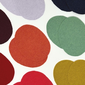 May include: A collection of colourful felt circles in shades of red, orange, green, and purple, set against a white backdrop. The felt circles are arranged in pairs and singles, highlighting their texture and colour variations. Suitable for craft projects.