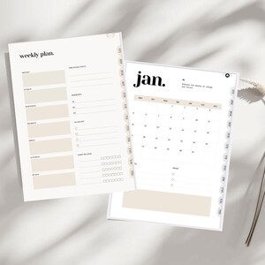 Puede incluir: Dos planificadores abiertos con una combinación de colores neutros. Uno muestra un diseño de plan semanal con secciones para cada día y notas. El otro muestra un calendario de enero con fechas y espacio para notas. El texto "weekly plan" y "jan." son visibles.