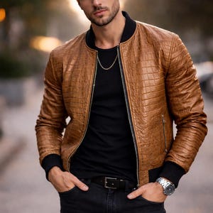May include: A brown leather jacket with a textured, crocodile-like pattern. The jacket has a black collar and cuffs, a zipper closure, and is worn over a black t-shirt. The person is also wearing black jeans and a silver watch.