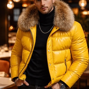 May include: A vibrant yellow puffer jacket featuring a fur collar, worn over a black turtleneck. The outfit includes black leather trousers, a silver chain, and a watch. The background is a blurred interior setting.