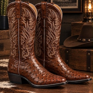 May include: A pair of brown leather cowboy boots featuring a distinct quill-patterned texture on the foot and shaft. The boots have a pointed toe, a stacked heel, and intricate light-colored decorative stitching along the upper shaft area.