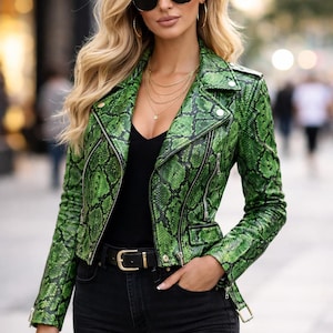 May include: A green snakeskin-effect leather jacket, black top, and black jeans. The jacket features a biker style with a notched collar, zip details, and a belt. The outfit is accessorized with sunglasses, gold jewellery, and a black belt.