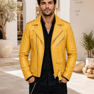 May include: A bright yellow motorcycle jacket with a textured ostrich-skin pattern, featuring silver-tone metal zips, a notched lapel, epaulettes on the shoulders, and a buckled belt at the waist, worn over a black button-down shirt and black trousers.