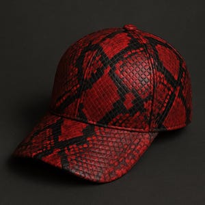 May include: A red and black patterned baseball cap. The cap features a snakeskin design with a curved brim and a rounded crown. The color scheme is primarily red with black accents.
