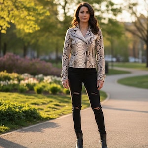 Pode incluir: Uma jaqueta de couro com padrão de pele de cobra com zíper prateado, combinada com jeans pretos rasgados e botinhas pretas. A jaqueta apresenta uma paleta de cores neutras bege, marrom e branco. O fundo mostra um parque com árvores e um caminho.