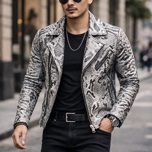 May include: A gray and white snakeskin-patterned leather jacket with a black t-shirt, black jeans, and a silver chain. The jacket has a classic biker style with a zipper closure and a notched collar. The person is wearing sunglasses and a watch.