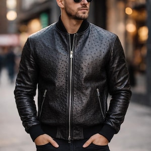 Pode incluir: Casaco bomber de couro preto com padrão texturizado, fecho de correr e bolsos laterais. O casaco tem gola e punhos canelados. A pessoa está usando jeans pretos e óculos de sol.