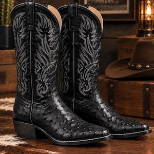 May include: A pair of black ostrich leather cowboy boots featuring a textured quill pattern on the foot, a pointed toe, and intricate grey stitching details on the tall shaft. The boots have a stacked heel and a classic western silhouette.