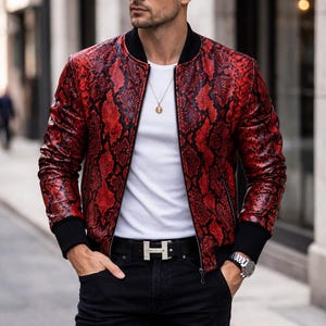 May include: Red snakeskin-patterned bomber jacket with black trim. The jacket is worn over a white t-shirt and black jeans. A silver belt buckle and a wristwatch are also visible.