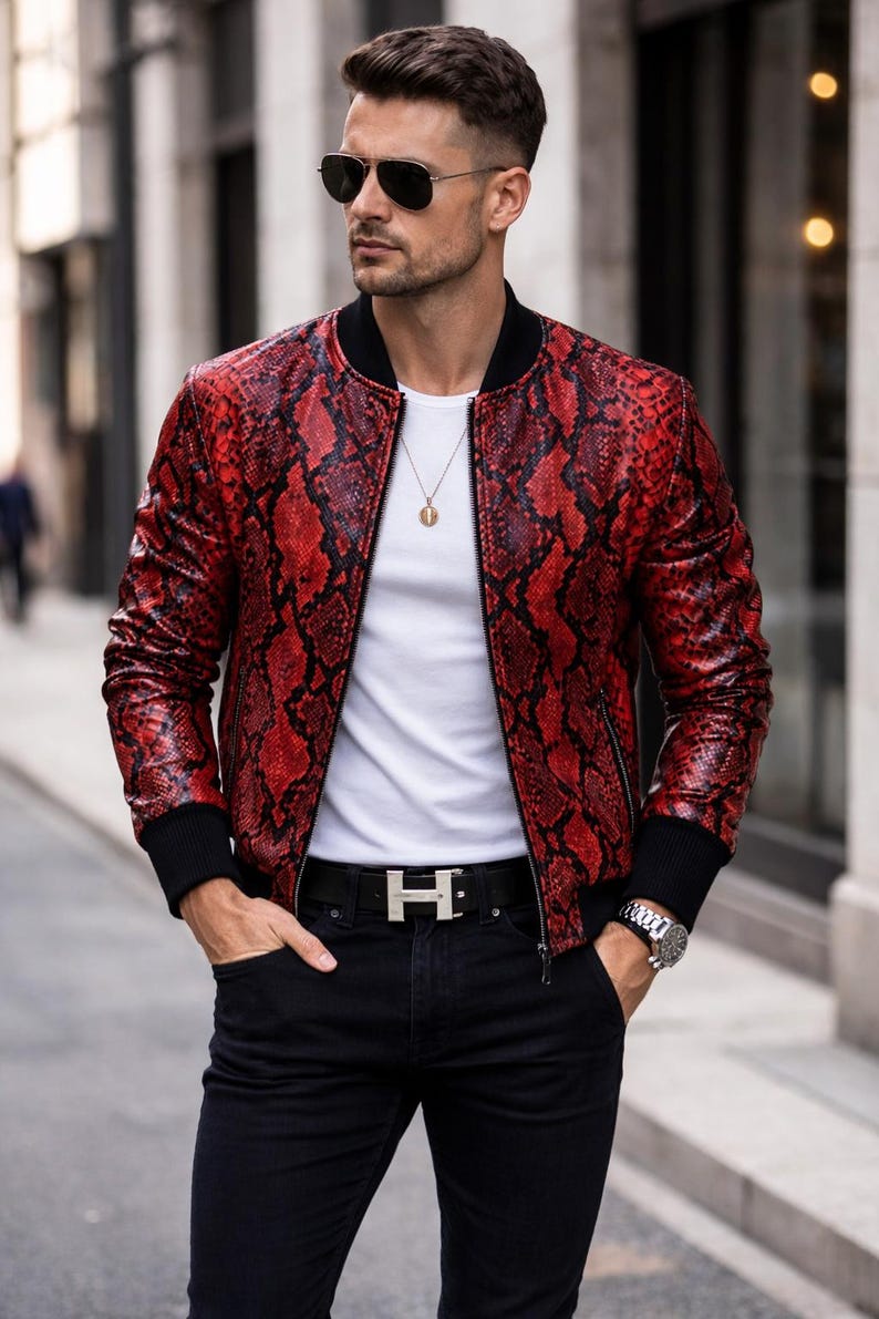 May include: Red snakeskin-patterned bomber jacket with black trim. The jacket is worn over a white t-shirt and black jeans. A silver belt buckle and a wristwatch are also visible.