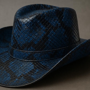 May include: A cowboy hat with a snakeskin pattern in shades of blue and black. The hat has a classic brim and a structured crown, offering a stylish accessory for various occasions. The hat is made of a textured material.