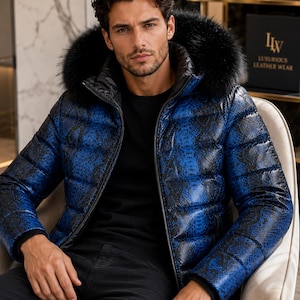 May include: A puffer jacket featuring a vibrant blue and black snakeskin pattern, a full-length front zipper, and a hood trimmed with thick black faux fur. The jacket is worn over a plain black long-sleeved shirt and black pants.