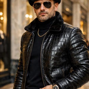 Pode incluir: Um homem usando um chapéu de pele preto com um emblema dourado, óculos de sol aviador e uma jaqueta de couro preta com padrão de crocodilo. Ele também está usando uma gola alta preta, corrente de ouro e um cinto com fivela dourada.