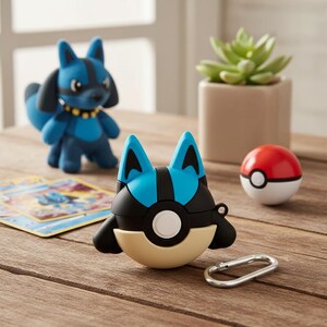 以下が含まれることがあります： 青と黒のキャラクターをテーマにしたAirPodケースとシルバーのカラビナクリップ。お揃いのフィギュアと赤と白のPoké Ballも表示されます。正方形のポットに入った小さな多肉植物が背景にあります。