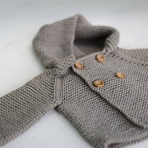 Puede incluir: Un cárdigan de punto gris con capucha y botones de madera.