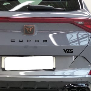 May include: Rear view of a gray SUV with the word "CUPRA" in black lettering. A bronze emblem is above the lettering. The model designation "VZ5" is in black on the right side of the vehicle.
