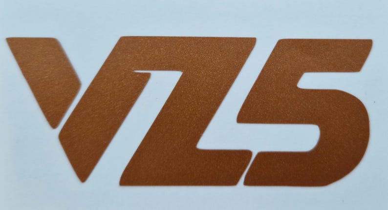May include: A copper-colored graphic of the letters "V75" on a white background. The numbers and letter are in a bold, sans-serif font. The image is a close-up, with the letters and numbers taking up most of the frame.