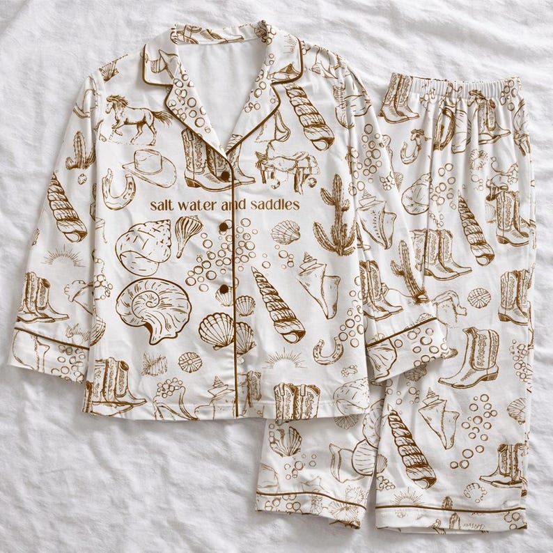 May include: White pajama set with a brown pattern of cowboy boots, seashells, horses, and cacti. The set includes a button-down top and matching pants. The text "salt water and saddles" is printed on the top.