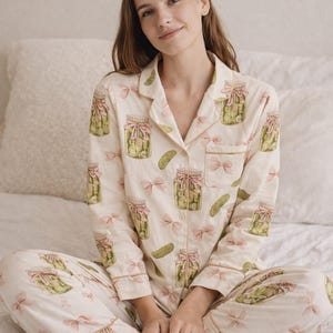 May include: Cream-coloured pyjama set with a pickle jar and bow pattern. The long-sleeved top and trousers have a repeating design of green pickles in jars with pink bows. The pyjamas have light brown trim.
