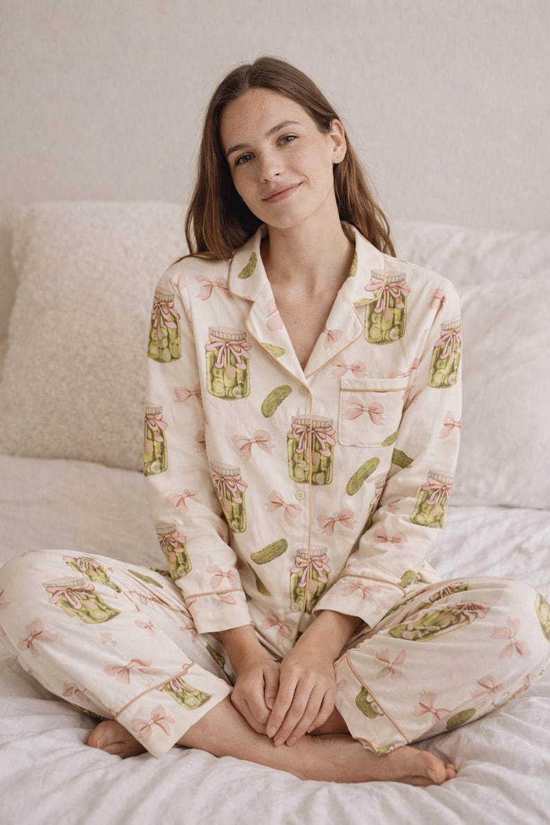 May include: Cream-coloured pyjama set with a pickle jar and bow pattern. The long-sleeved top and trousers have a repeating design of green pickles in jars with pink bows. The pyjamas have light brown trim.