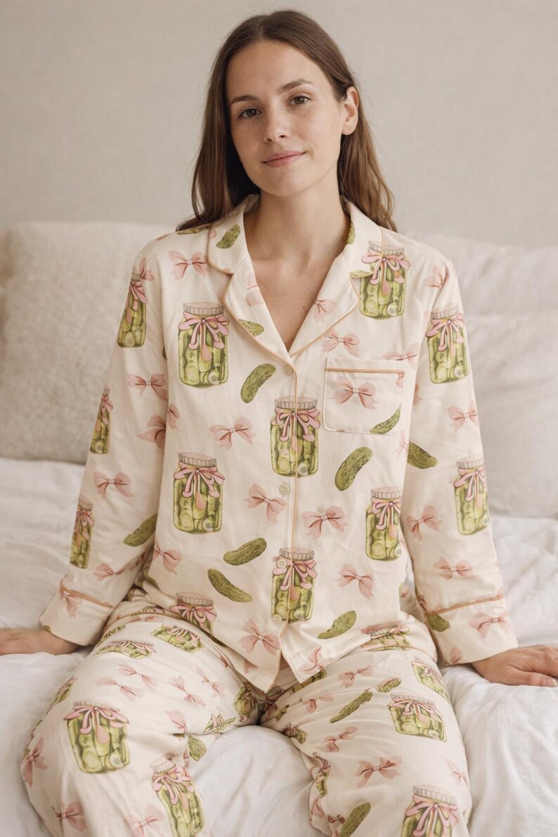 May include: Cream-coloured pyjama set with a repeating pattern of pickle jars and pink bows. The long-sleeved top and trousers have light brown trim. The pyjamas are made of a soft, comfortable material.