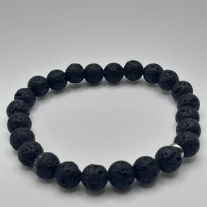 Peut inclure: Un bracelet de perles en pierre de lave noire. Le bracelet est composé de perles rondes et poreuses, assemblées avec une perle d'accentuation argentée. Les perles ont une surface texturée et sont de couleur charbon foncé.