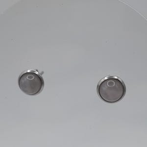 Peut inclure: Une paire de boucles d'oreilles à clous. Chaque boucle d'oreille présente une pierre rose pâle ronde sertie dans une lunette de couleur argentée. Les boucles d'oreilles sont présentées sur un fond clair et uni.