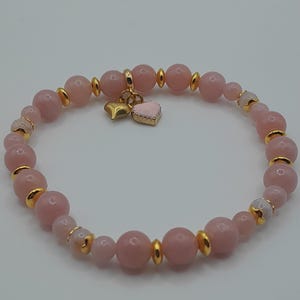 Peut inclure: Un bracelet de perles roses avec des accents dorés et un charm en forme d'étoile dorée et de cœur rose. Le bracelet est composé de perles rondes rose clair et d'entretoises dorées.