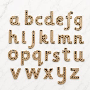 May include: A set of twenty-six lowercase alphabet letters made of light brown material. Each letter features black dashed lines and directional arrows with numbered steps to guide the writing stroke, arranged in four rows from a to z.
