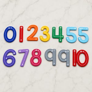 May include: A set of colourful wooden numbers from zero to ten, each featuring white dashed directional lines and arrows to guide writing. The digits are displayed in various colours including blue, red, orange, yellow, green, purple, pink, and grey.